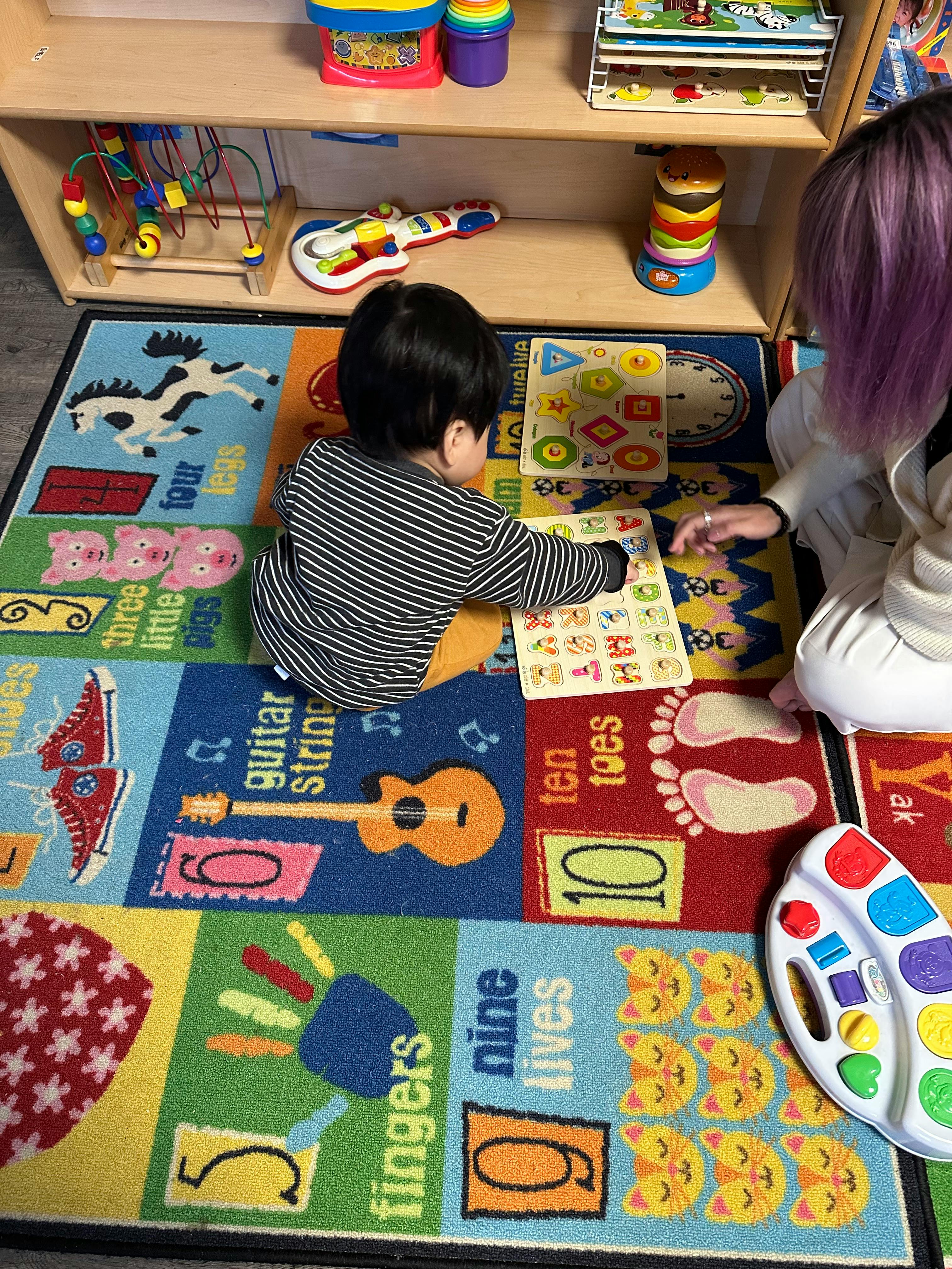 Child and person playing with puzzles on a colorful rug
