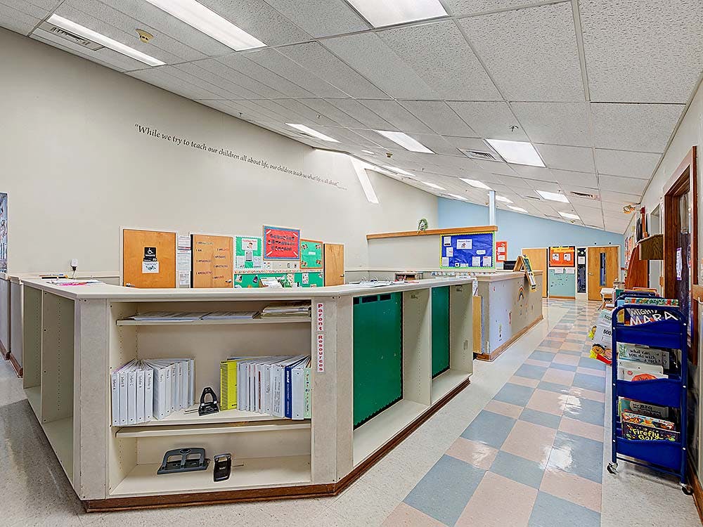 An empty classroom with cubbies and a low bookshelf, a wall quote