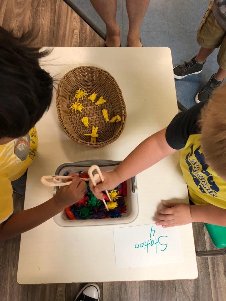 Two children using tongs to pick up colorful objects from a bin