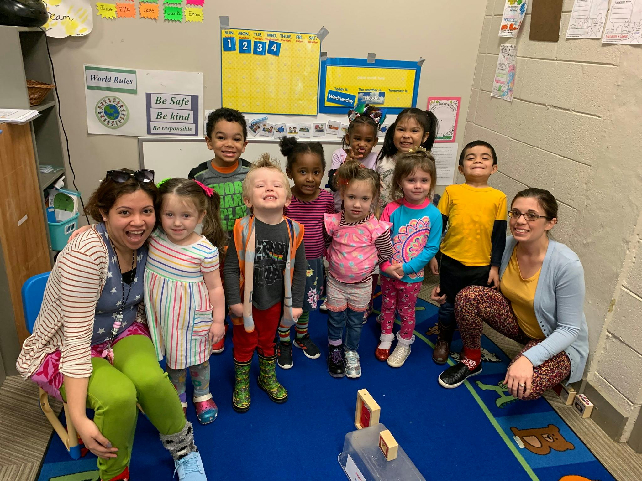 Two adults and multiple children posing for a photo in a classroom