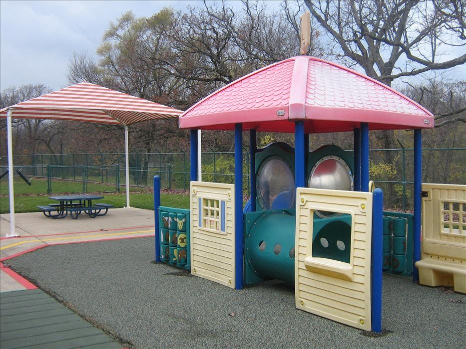 A playground with a red and white striped canopy over a picnic table and a pink-roofed play structure