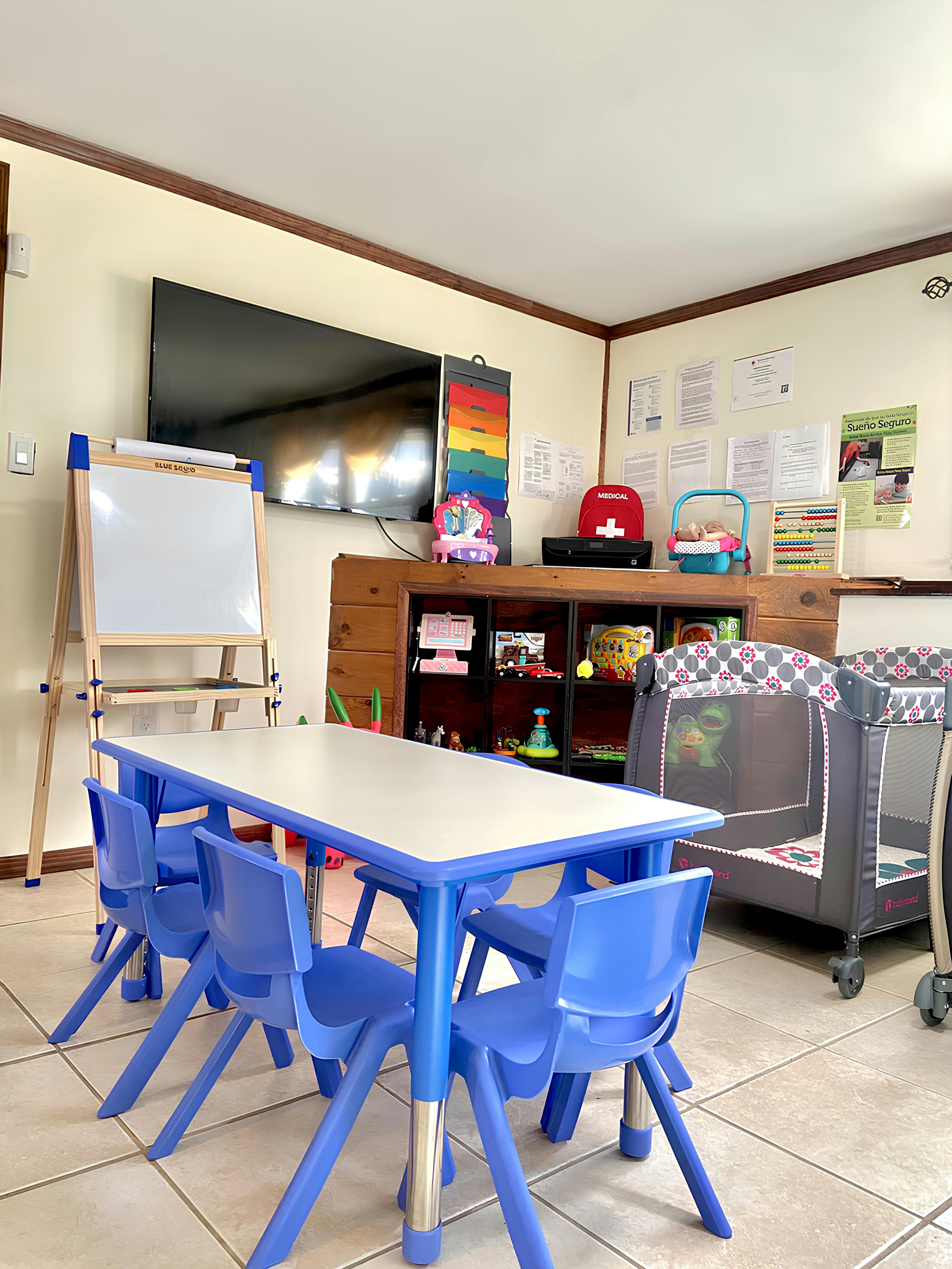 Children's classroom with blue table and chairs, easel, and playpen