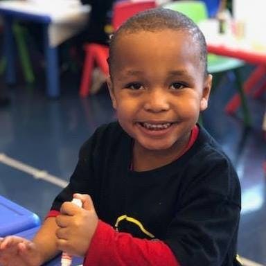 Child smiling and holding a marker in a classroom