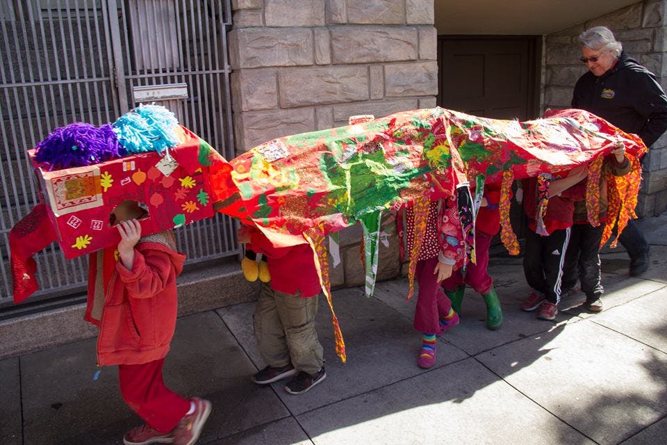 Children and an adult carrying a colorful, decorated parade float