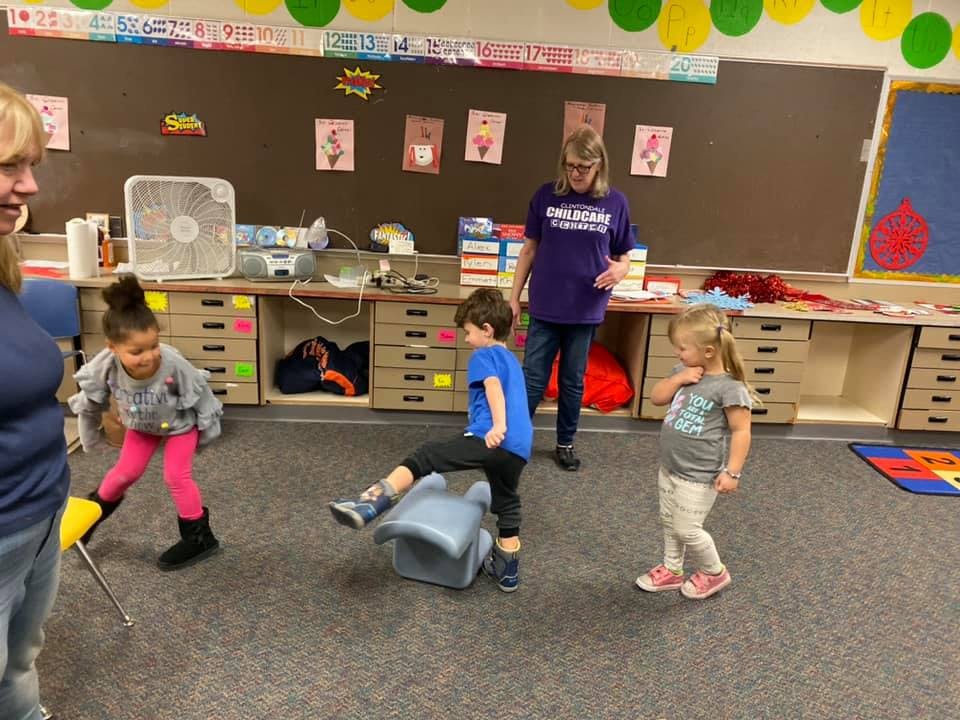 Adults and children in a classroom, one child kicking a soft toy