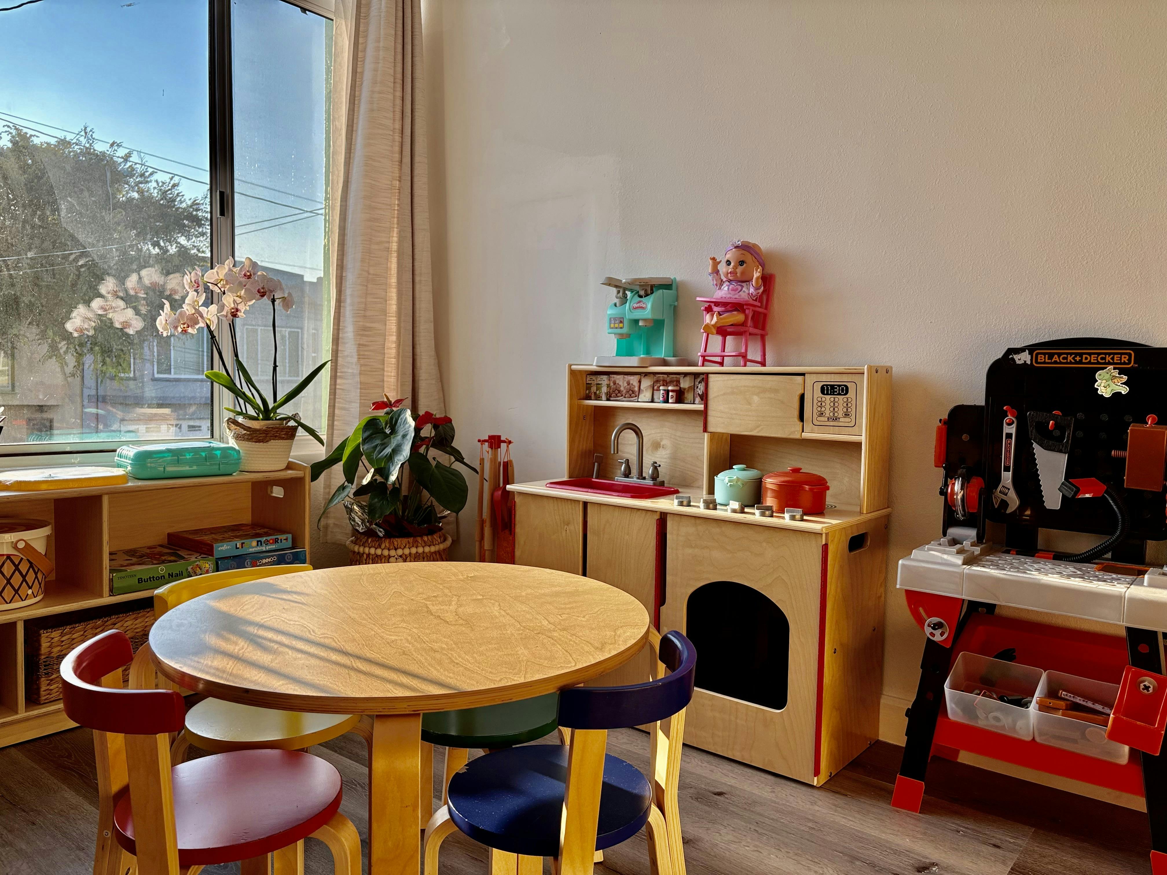 Playroom with a small wooden table and chairs, toy kitchen, and workbench