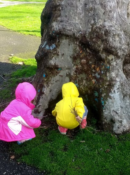 Two children in raincoats playing by a tree