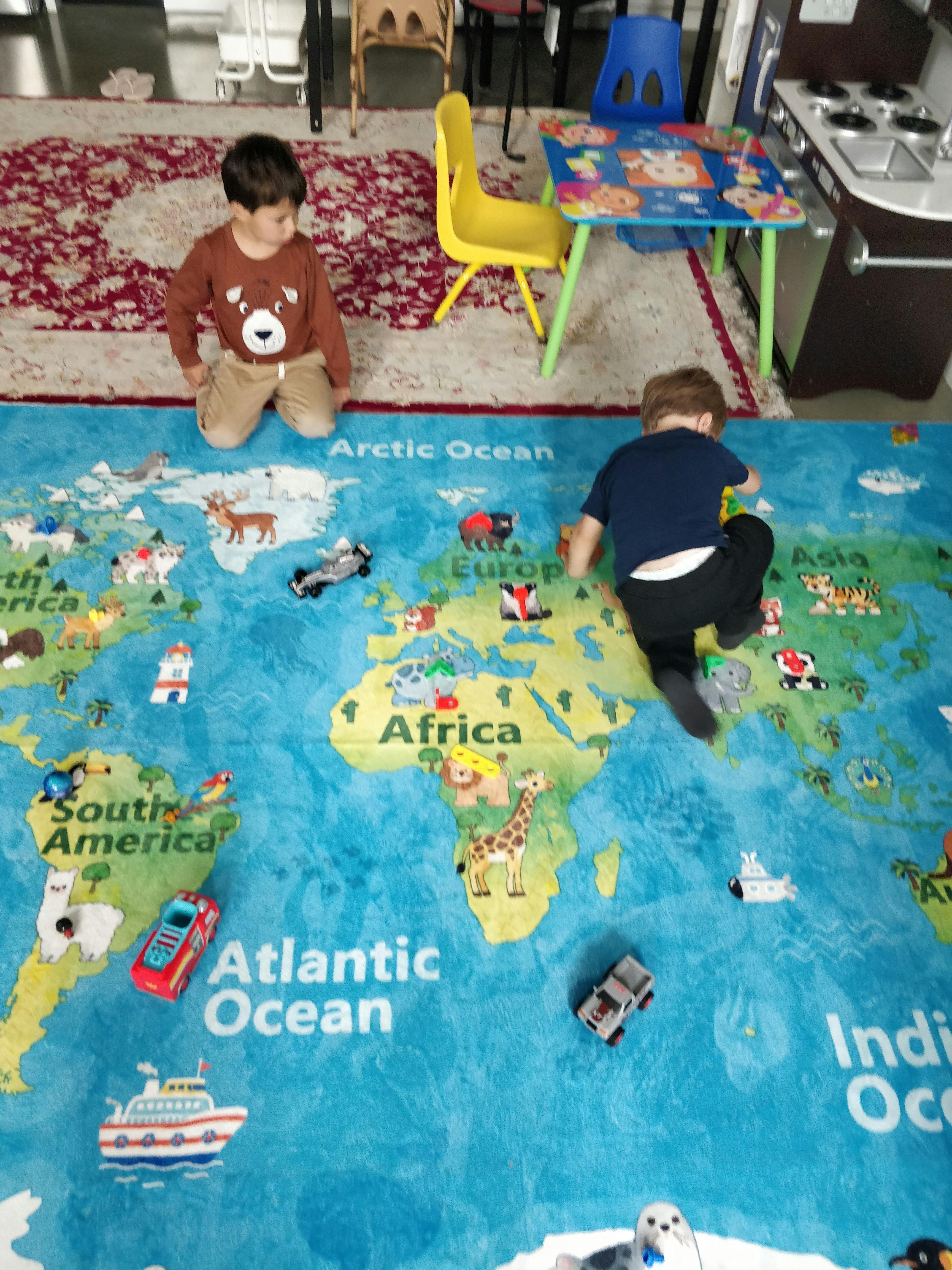 Two children playing with toy cars on a large world map rug