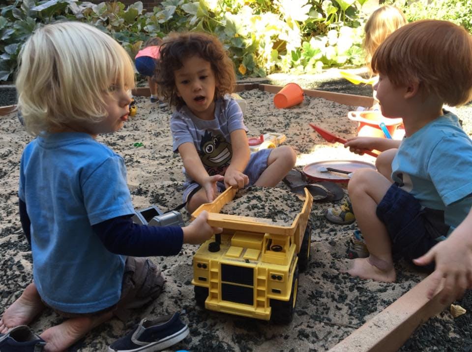 Three children playing in a sandbox with a toy dump truck