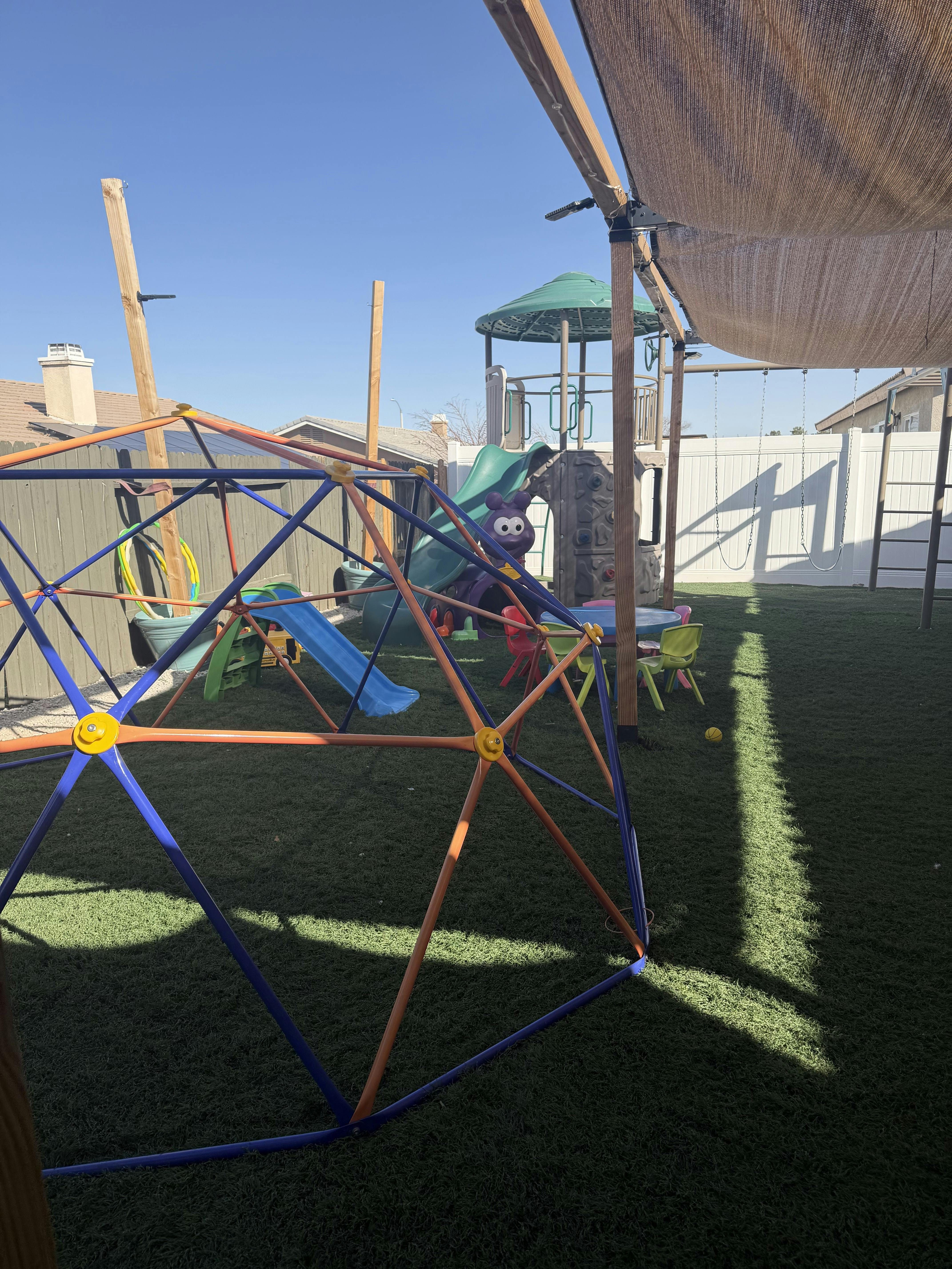 Playground with dome climber, slide, and swing set on artificial turf