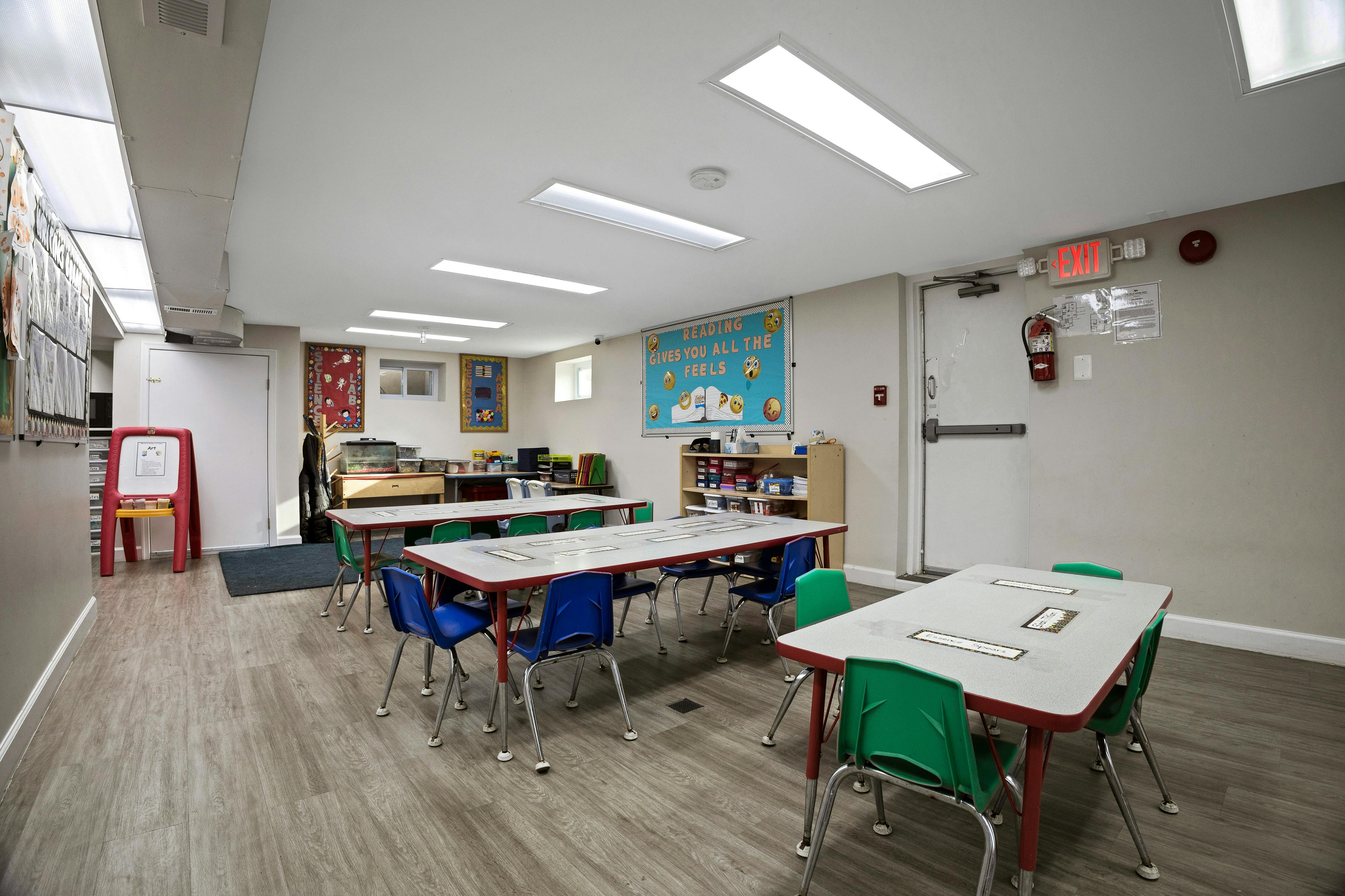 Classroom with multiple long tables and chairs, bulletin boards, and an exit sign