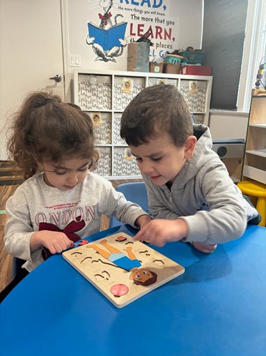 Two children playing with a puzzle on a blue table