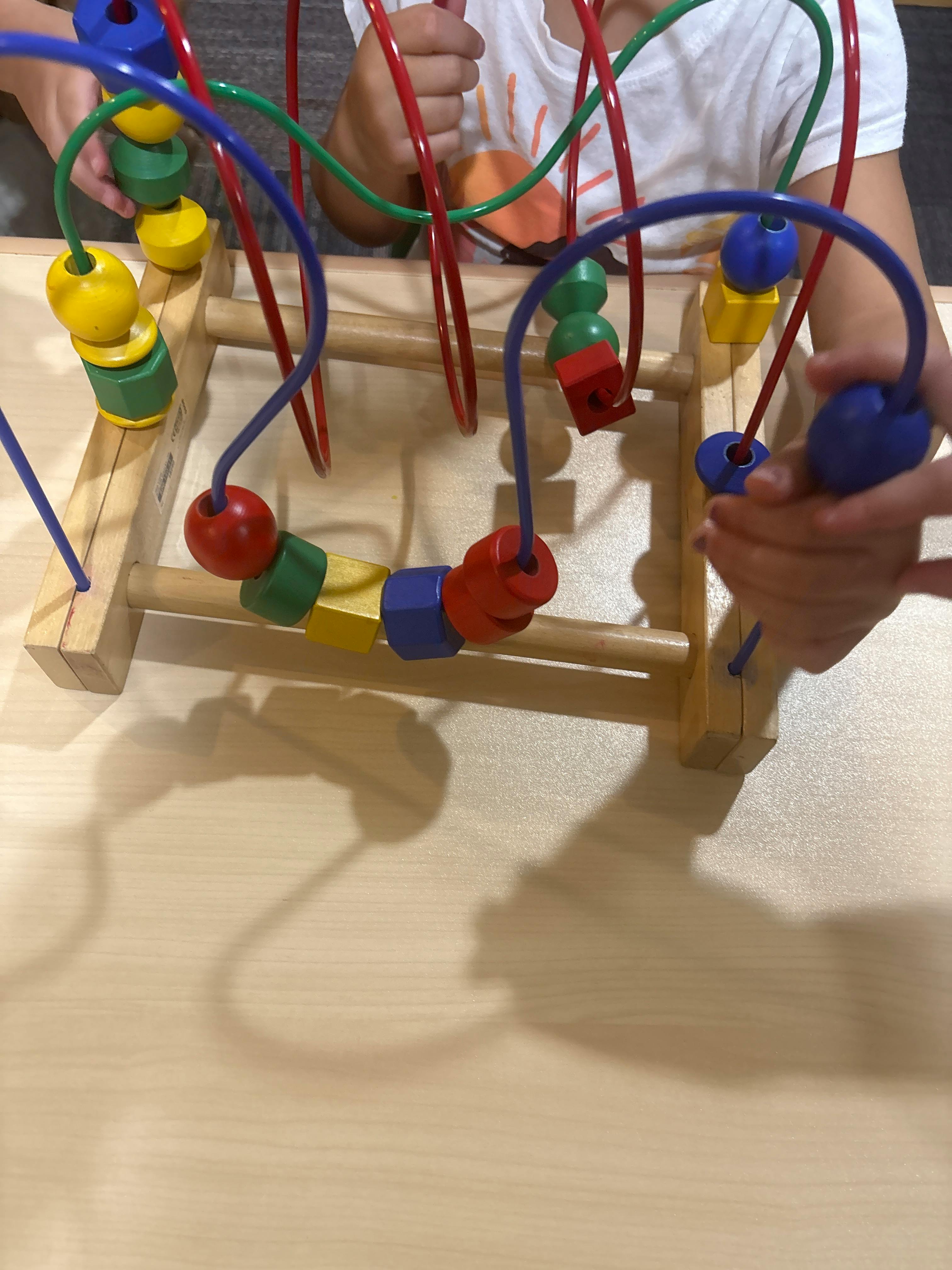 Two people playing with a colorful bead maze toy
