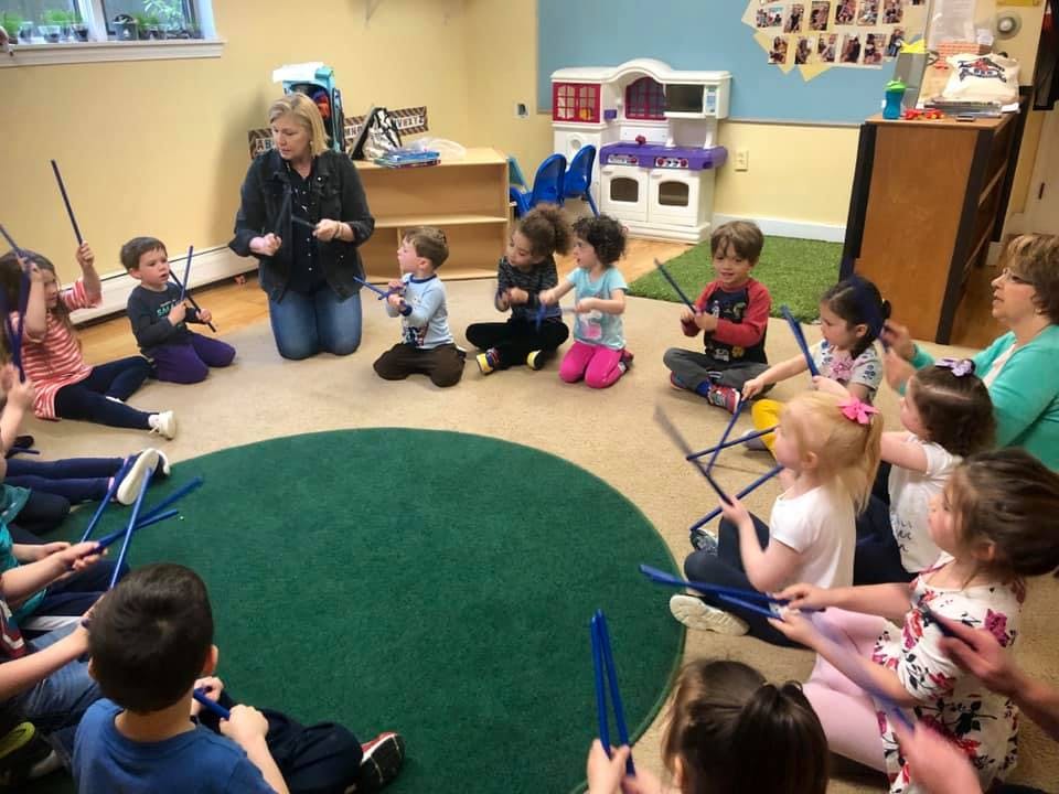 Adult and children sitting in a circle playing with sticks in a classroom