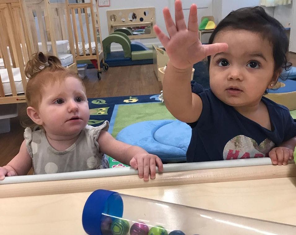 Two children in a playpen, one raising a hand