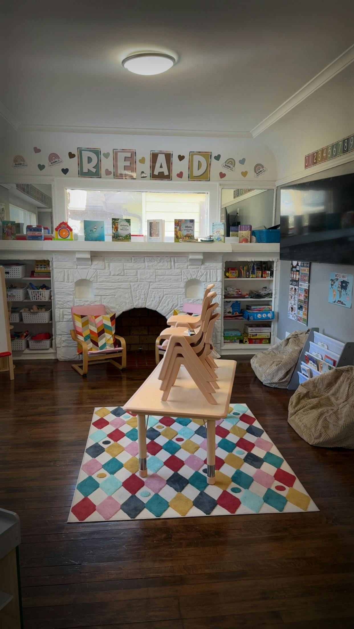 Classroom with a colorful rug, small table with stacked chairs, and a fireplace