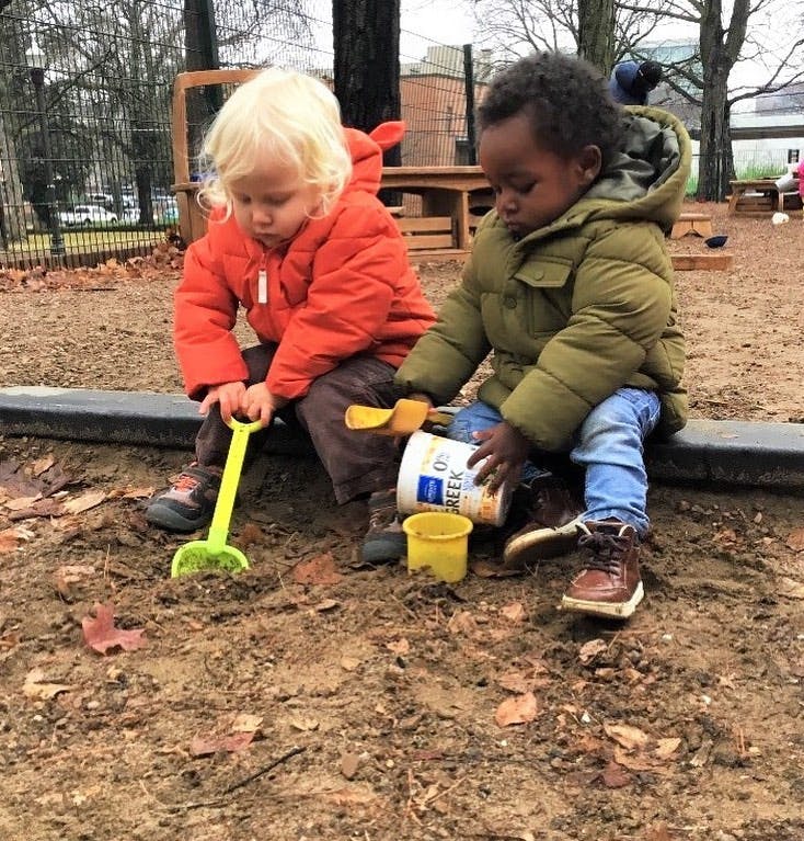 Two children playing in dirt with a shovel and containers
