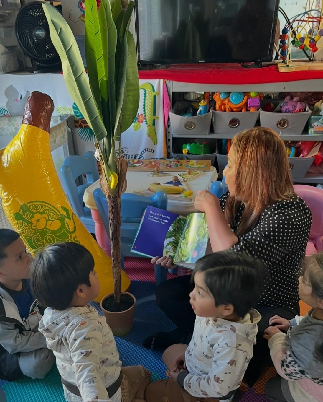 Person reading a book to four children sitting on the floor in a classroom