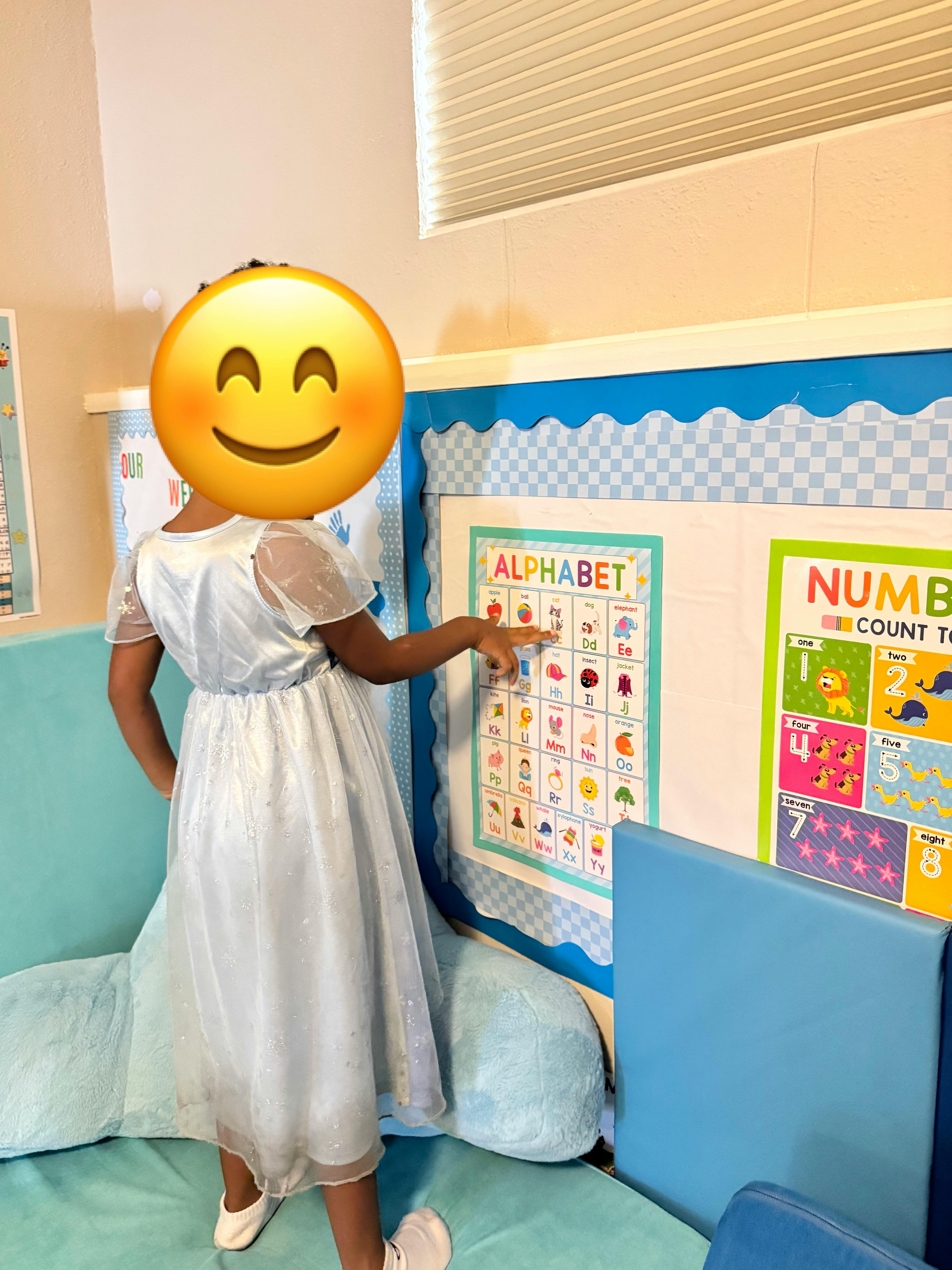 Child pointing at an alphabet poster on a classroom wall