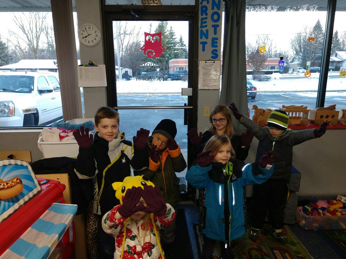 Group of children and an adult wearing winter clothing and gloves, waving