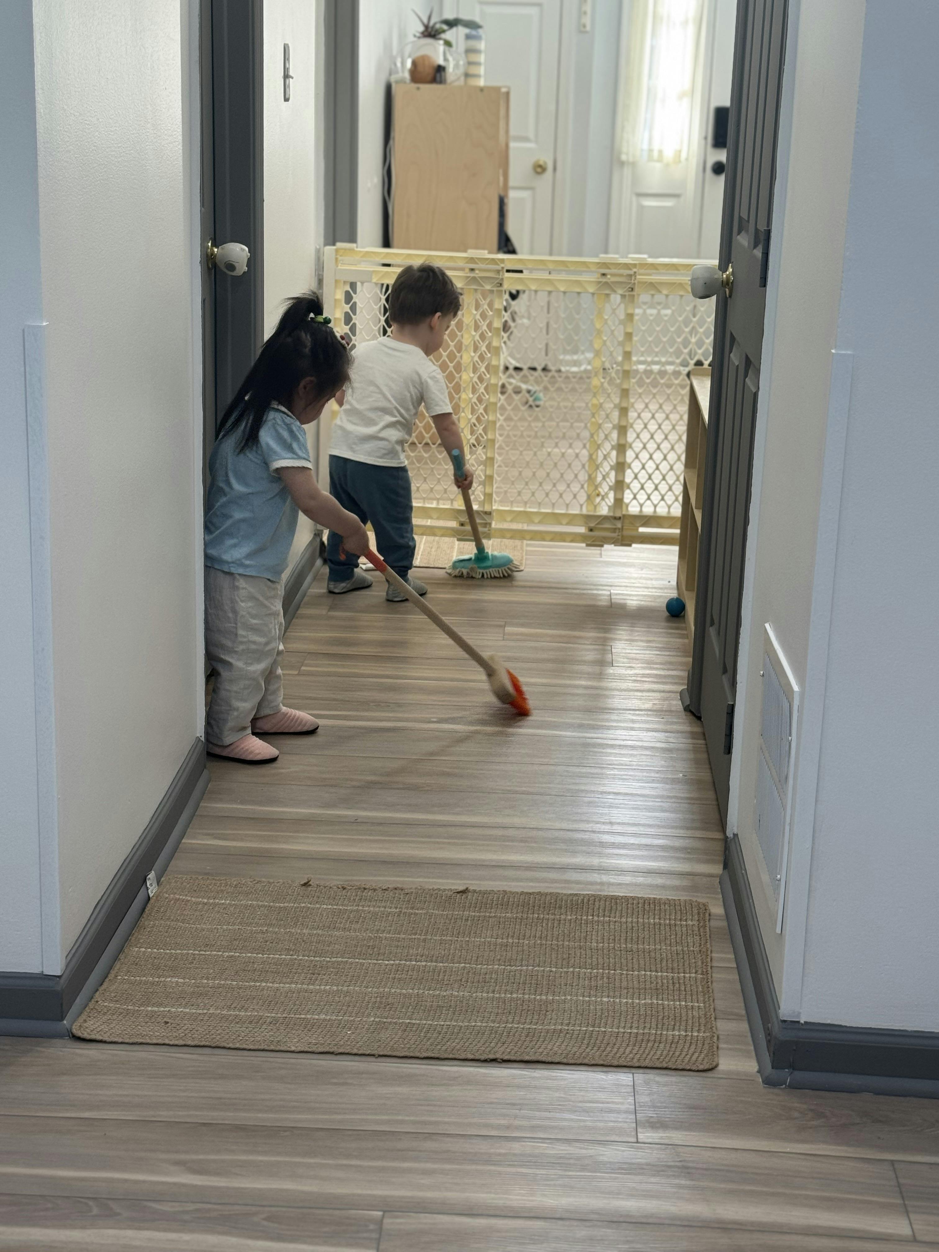 Two children using toy cleaning tools on a hallway floor
