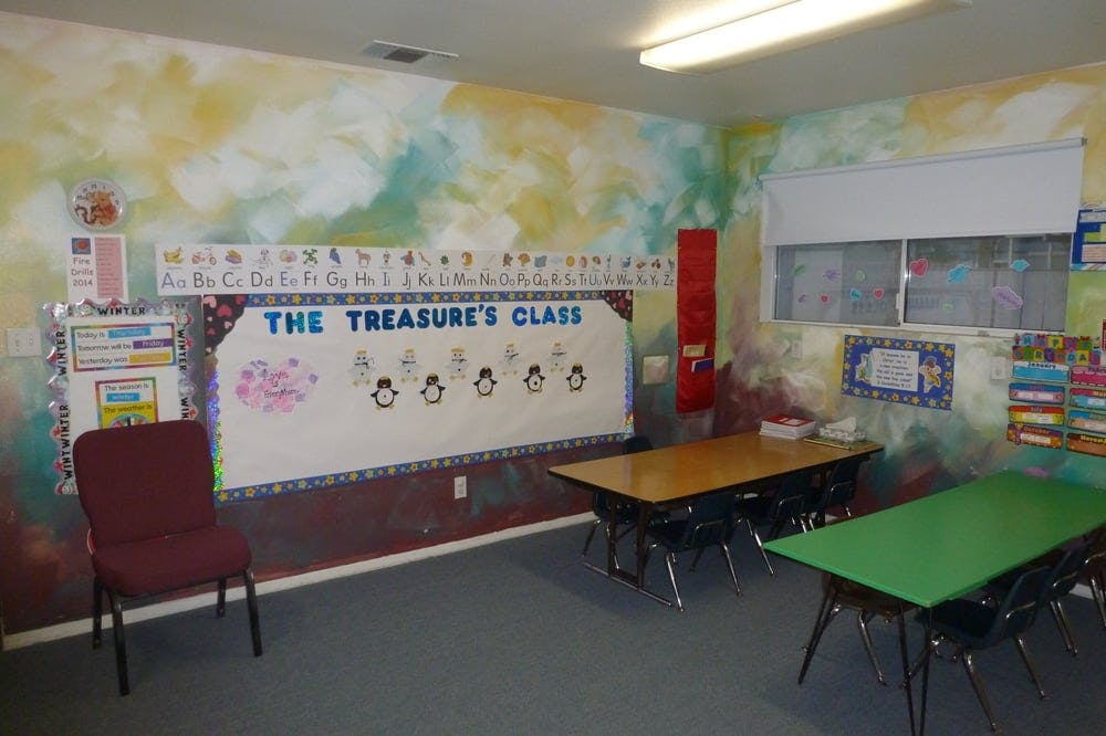 Classroom with tables, chairs, and a bulletin board that says "The Treasure's Class"