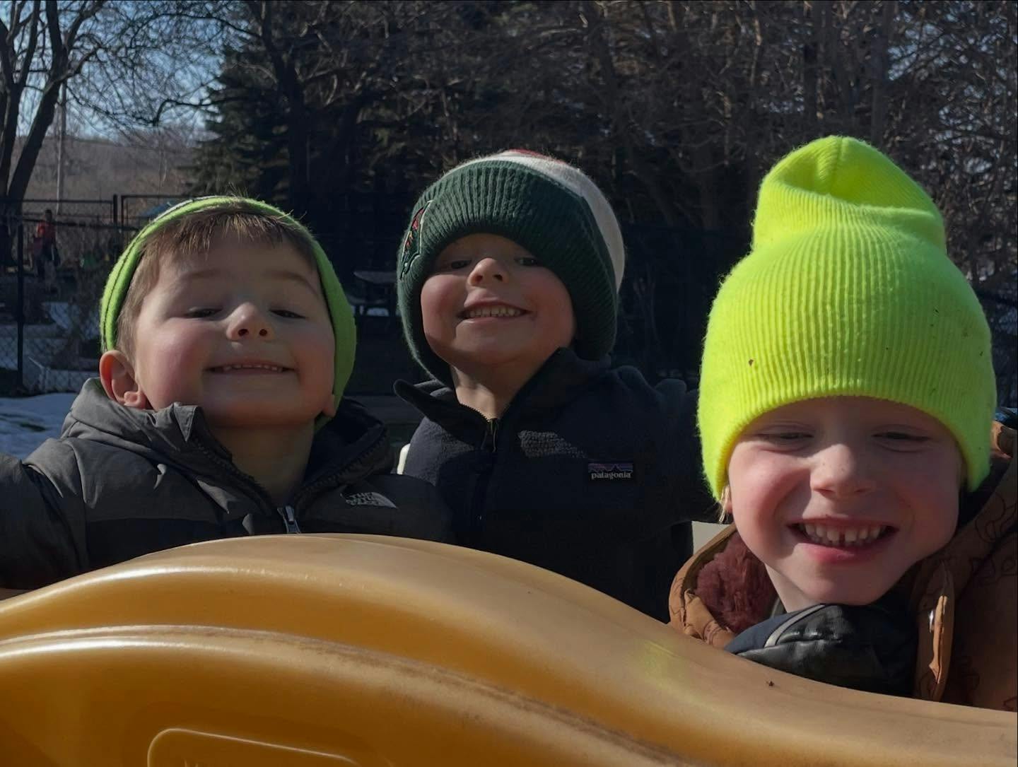 Three children in winter hats on a playground slide