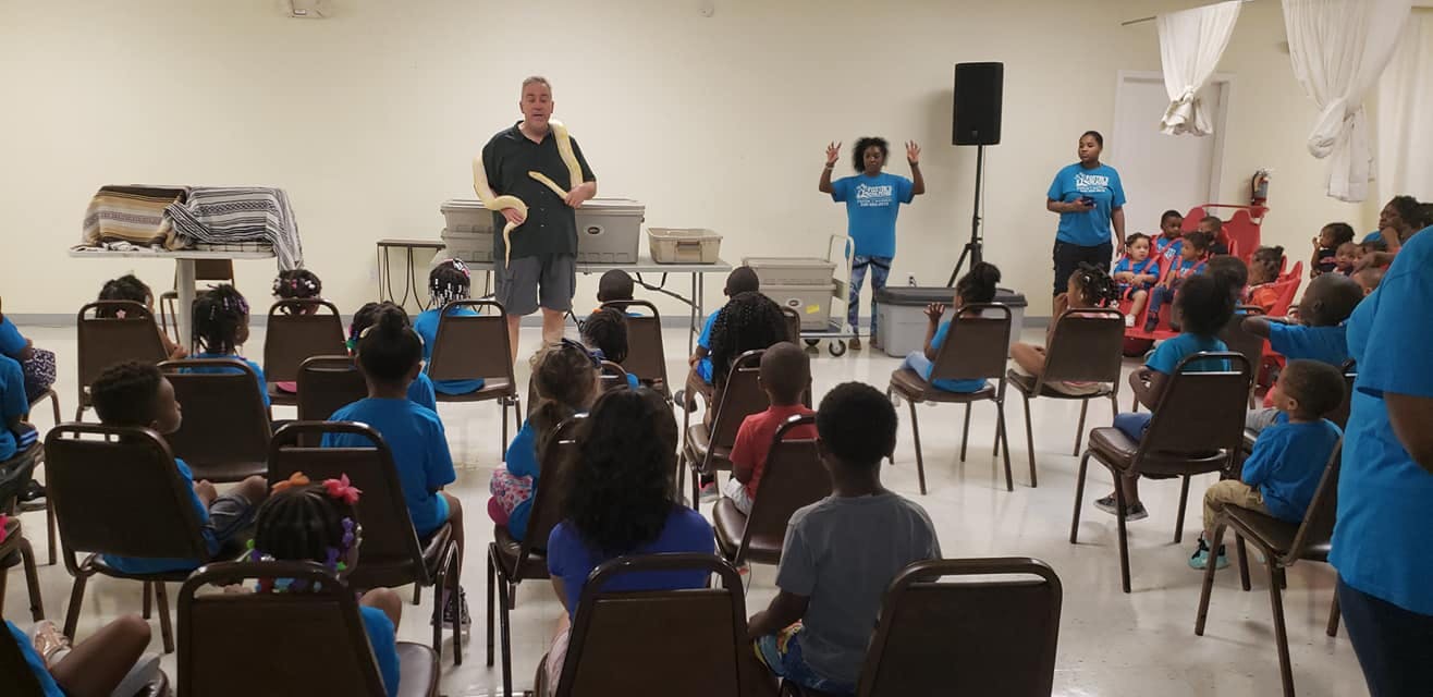 Adults presenting to a group of children and teens seated in chairs