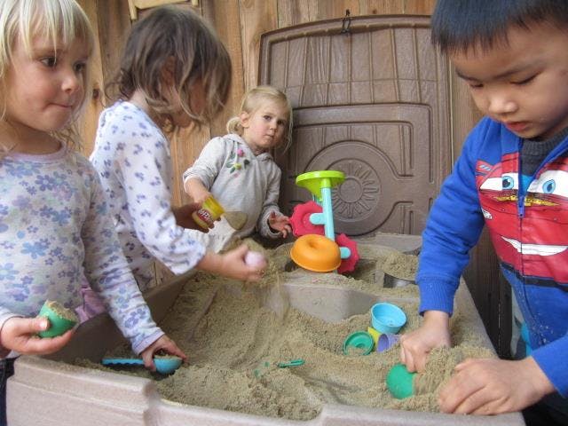 Children playing in a sandbox with sand and toys