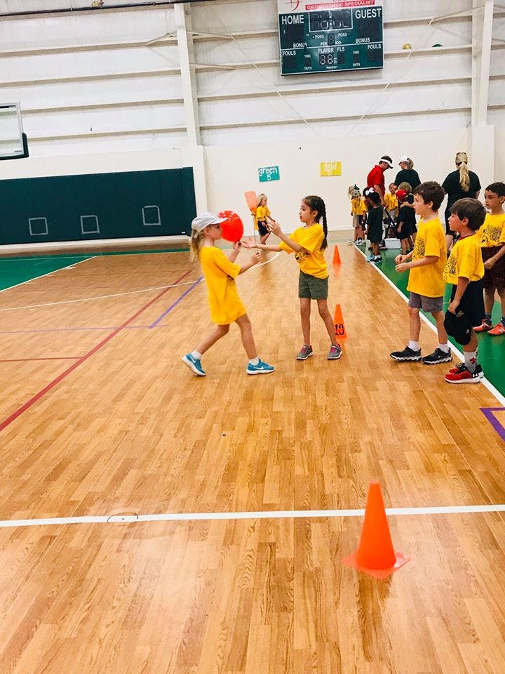 Two children playing with a red ball in a gymnasium