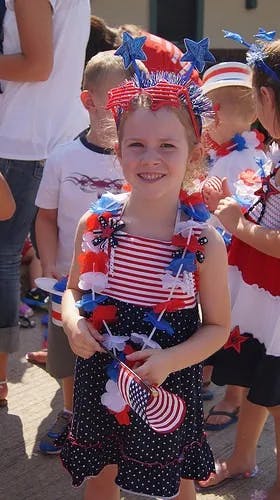 Child in patriotic headband and lei holding a small American flag