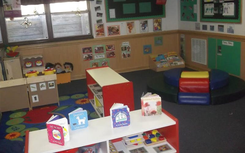 A classroom with a small play kitchen, bookshelves, and reading nook