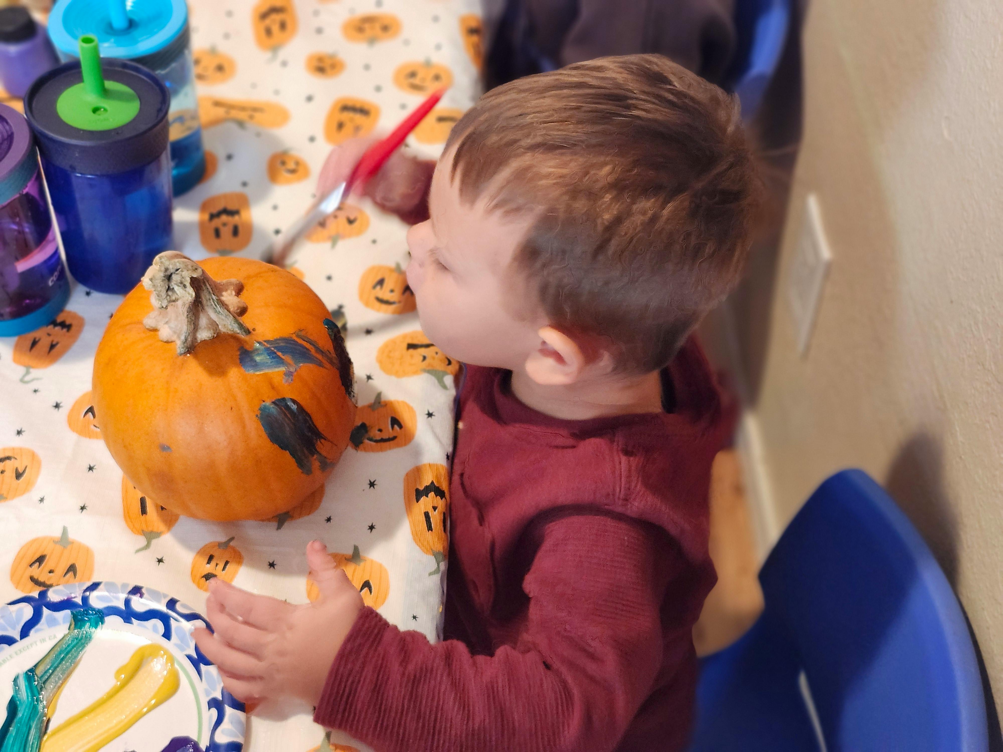 Child painting a pumpkin on a Halloween-themed tablecloth