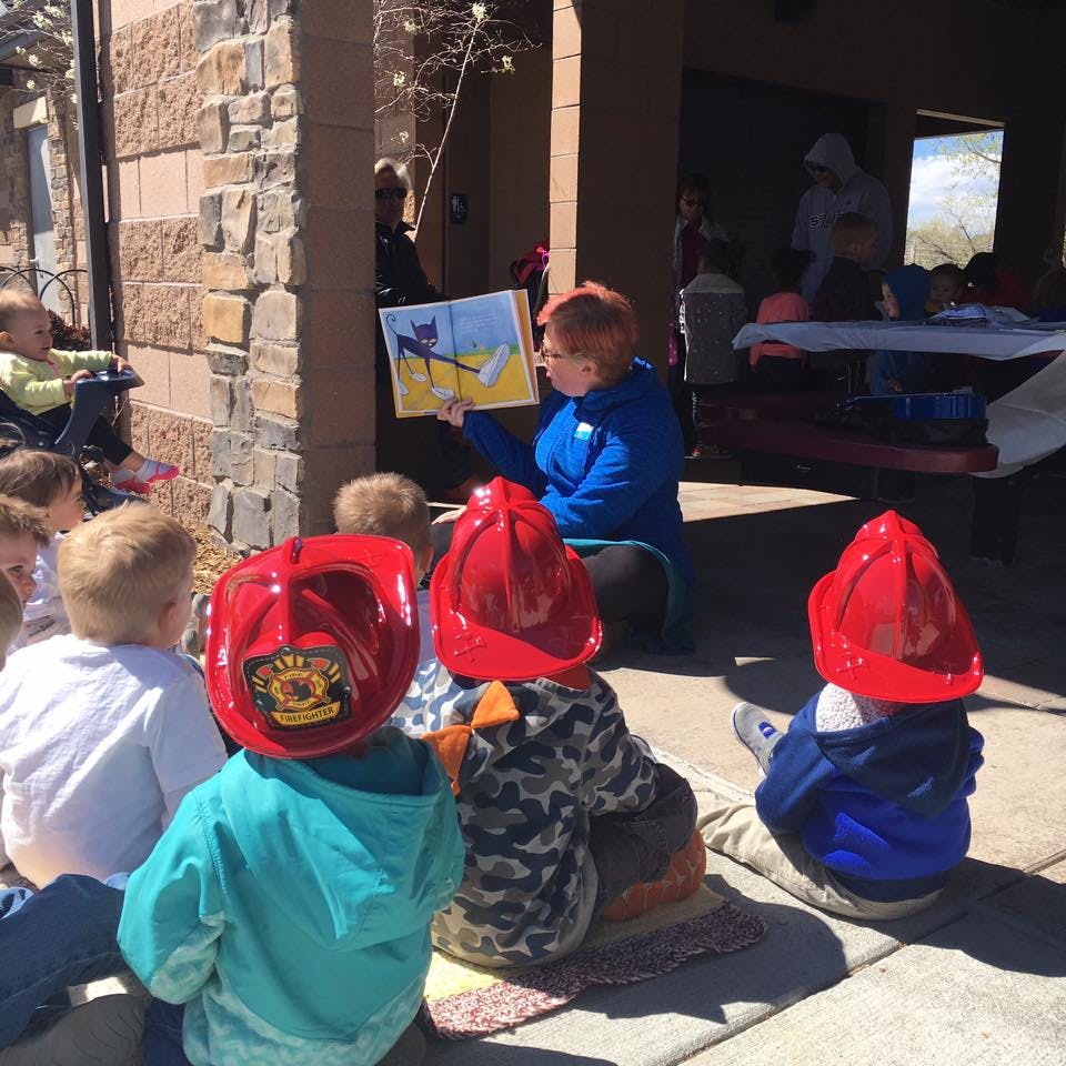 Person reading a book to children wearing red firefighter hats