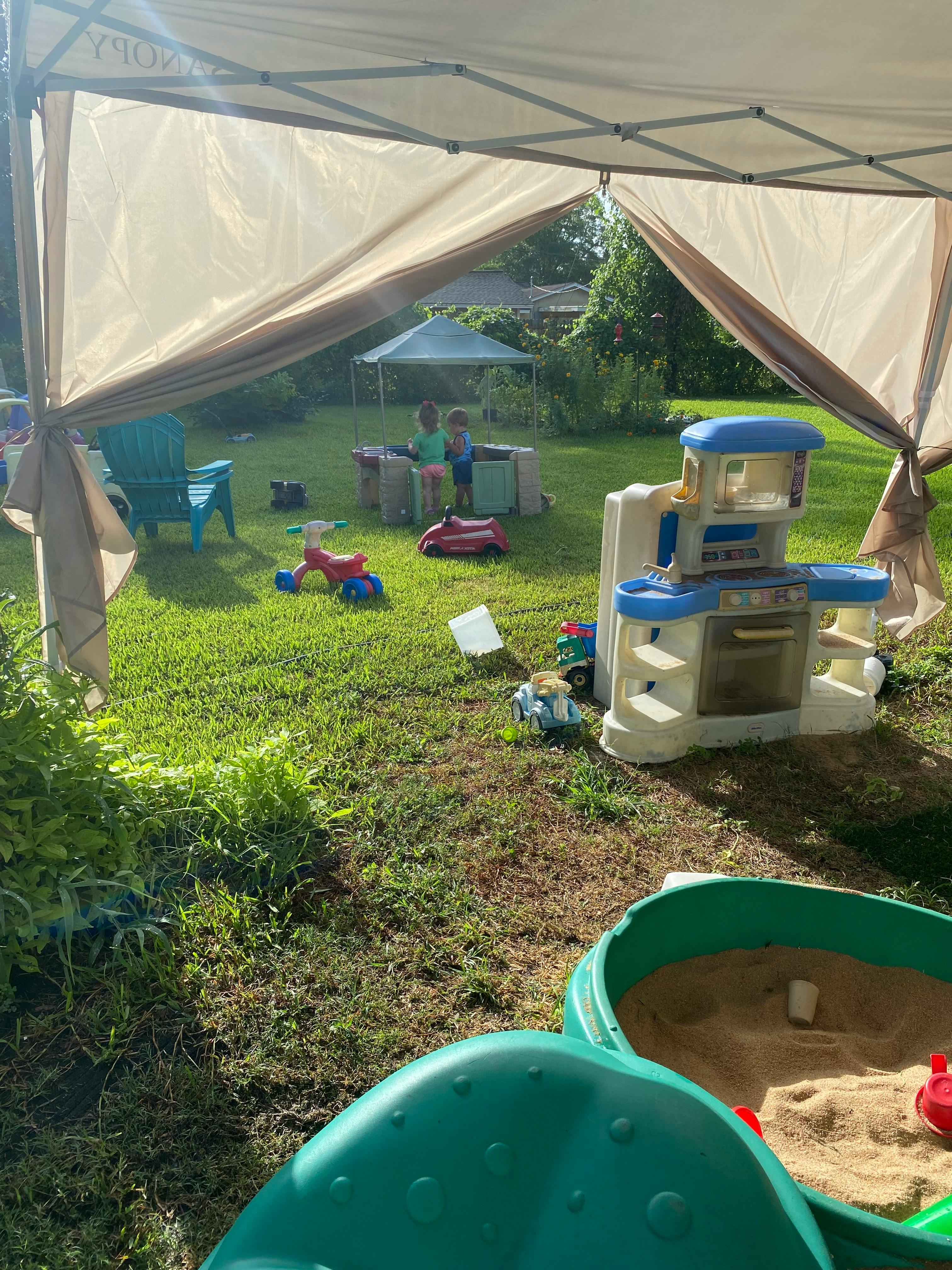 Two children playing in a backyard with toys and a sandbox