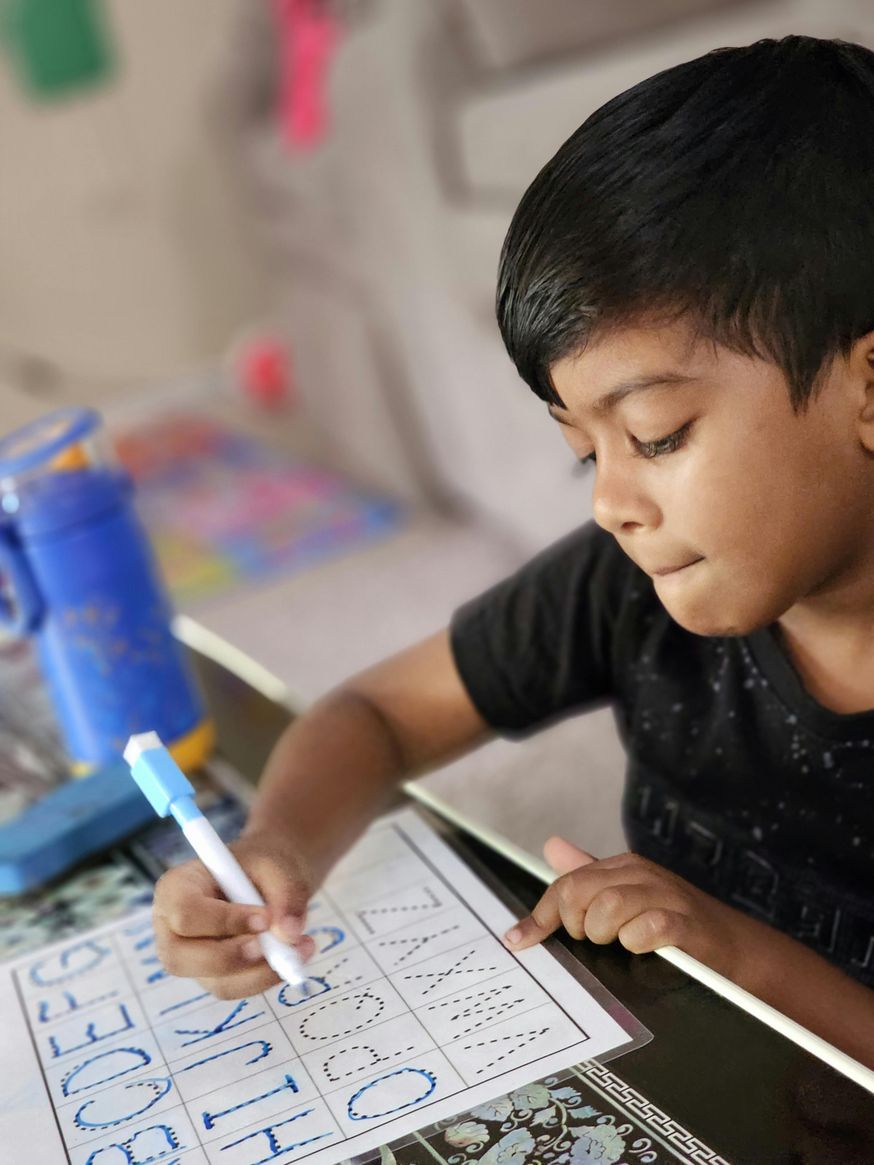 Child tracing letters on a worksheet with a marker