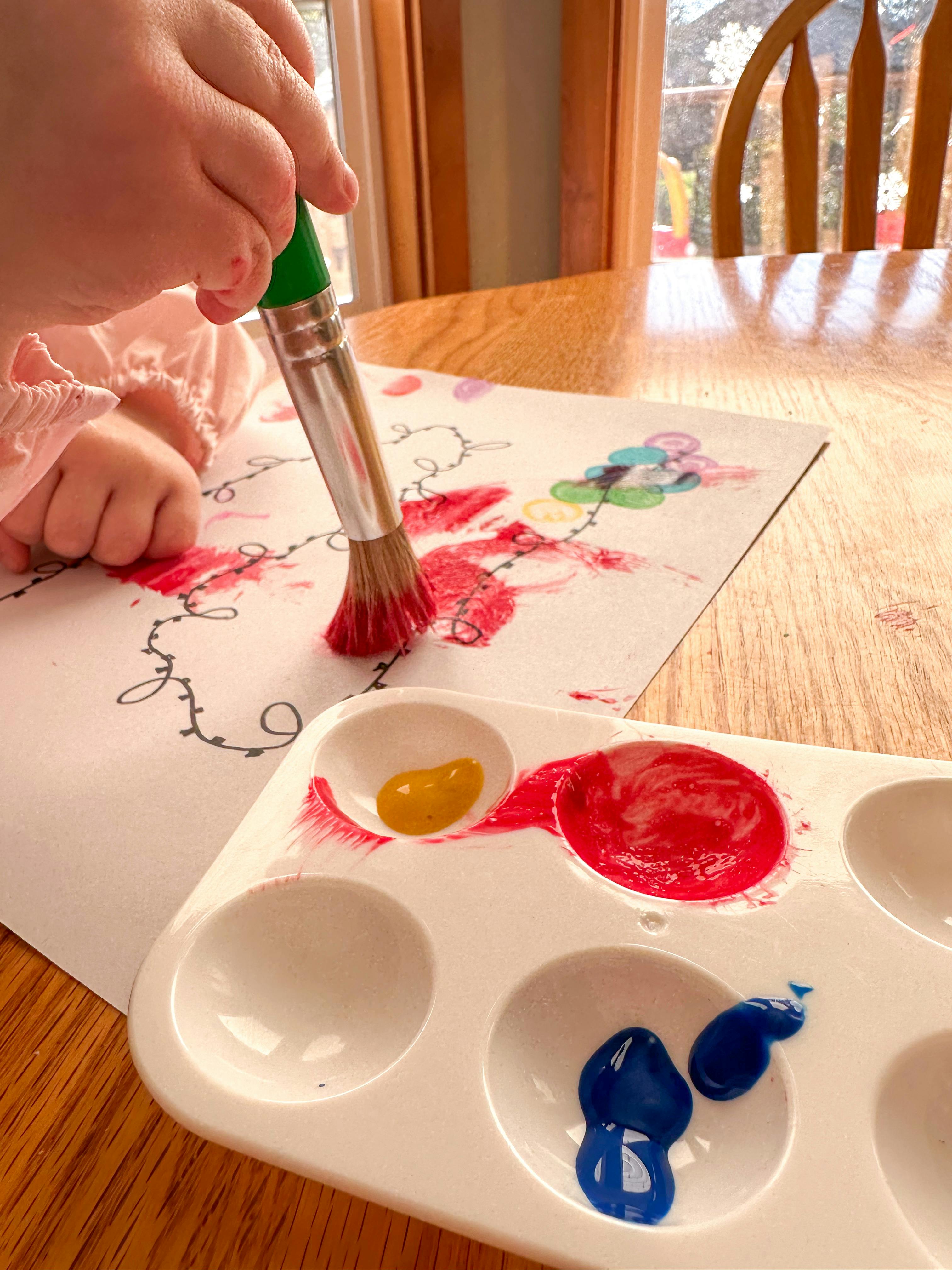 Child's hand holding a paintbrush over a painting and palette