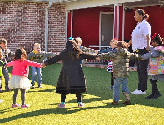 Children and an adult holding hands in a circle outdoors