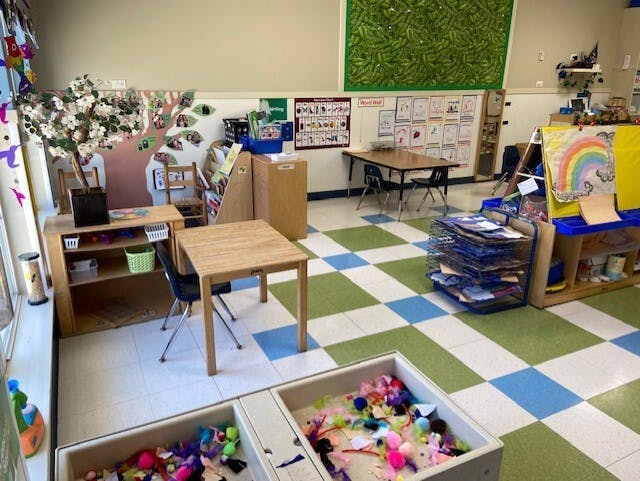 An empty classroom with small tables, chairs, and learning materials