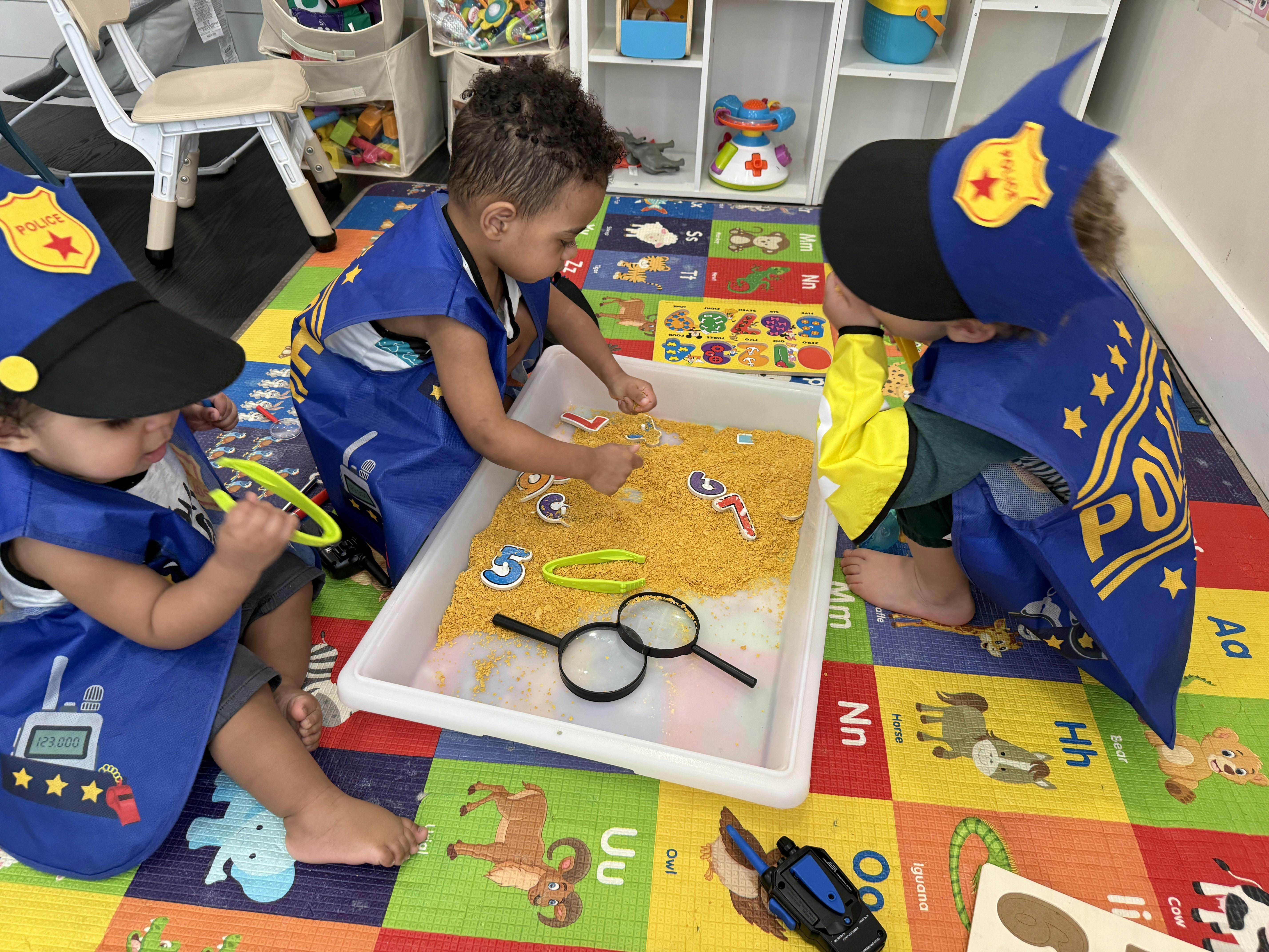 Three children wearing police costumes playing with numbers in a sensory bin