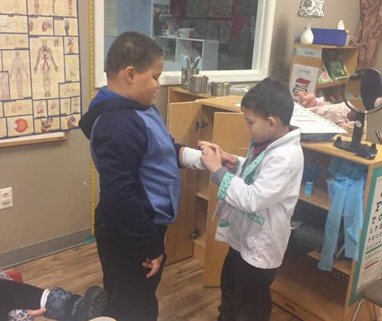 Child in white coat examining another child's arm