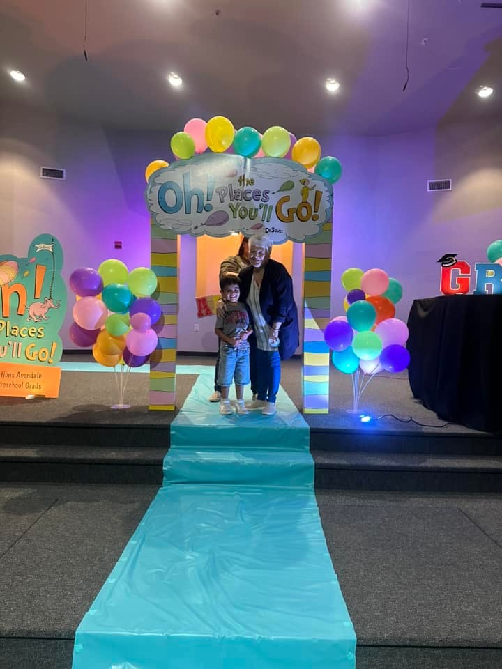 A person and a child standing under a balloon arch decorated for graduation