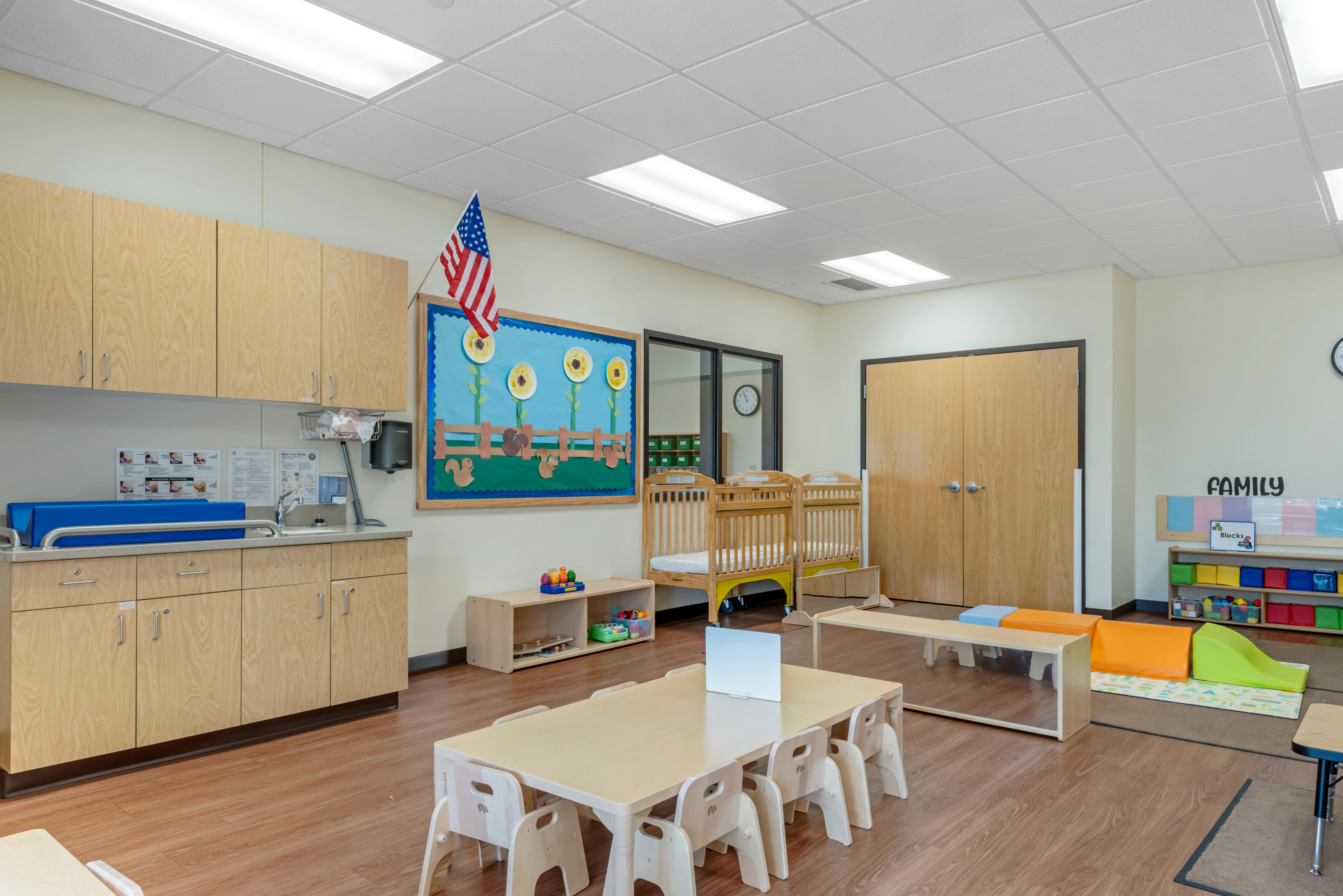 Classroom with changing table, two cribs, child-sized tables and chairs