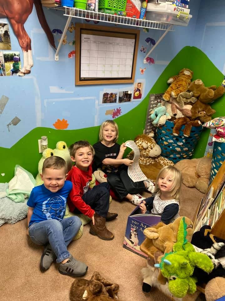 Four children sitting on the floor surrounded by stuffed animals