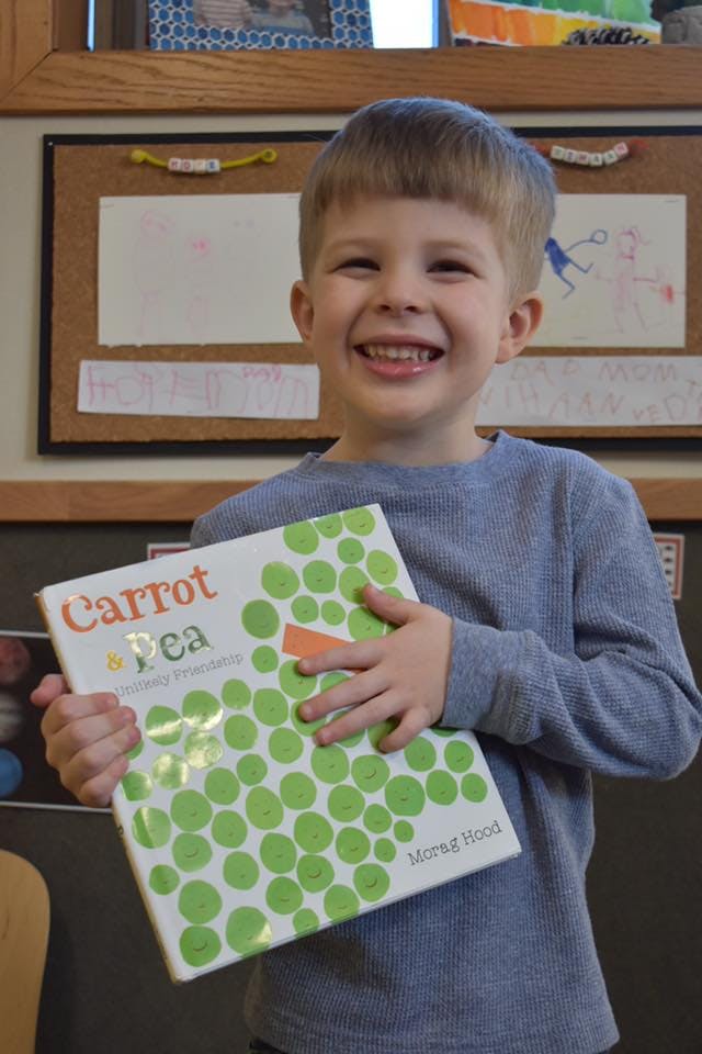 Child holding a book titled "Carrot and Pea"