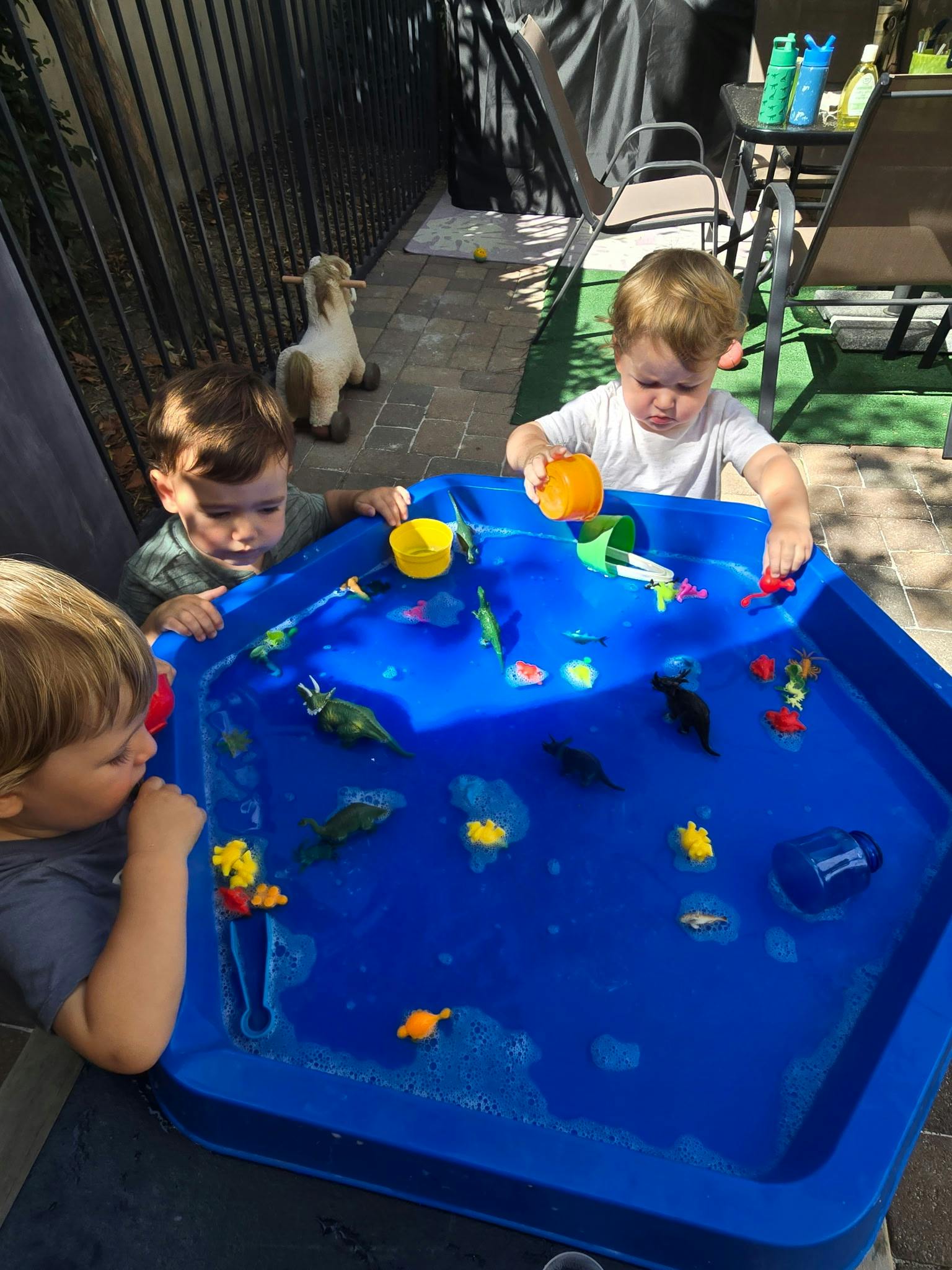 Three children playing with toy dinosaurs in a blue water activity table