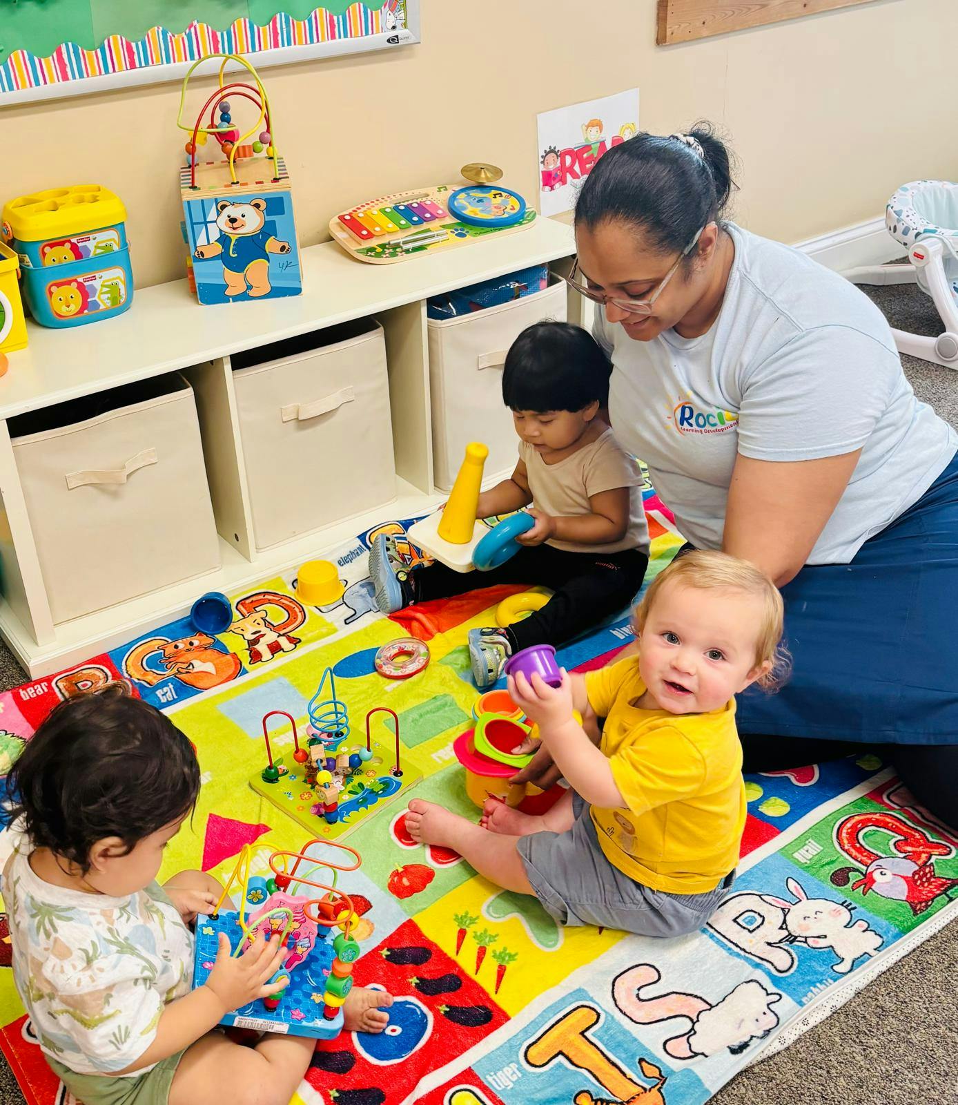 Adult and three children playing with toys on a colorful mat