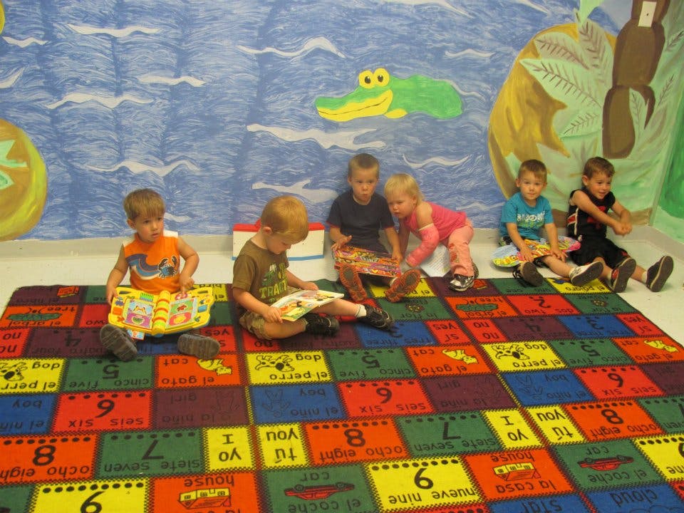 Children sitting on a colorful rug, some reading books