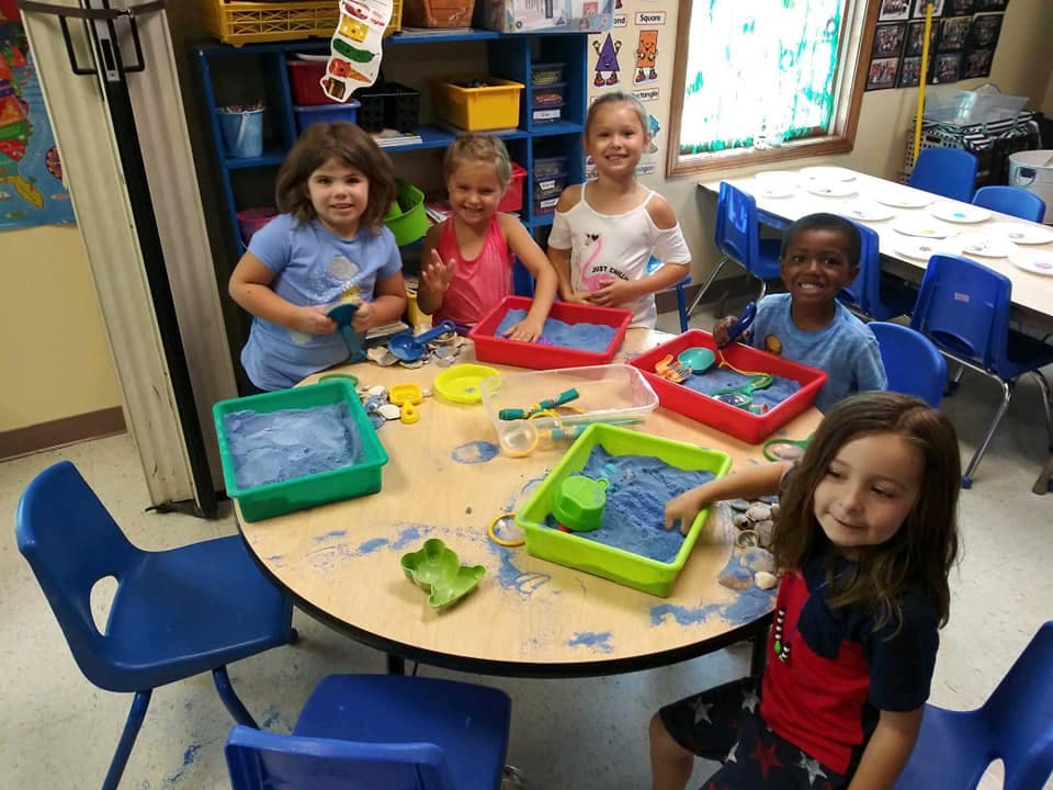 Children playing with sand and toys at a table