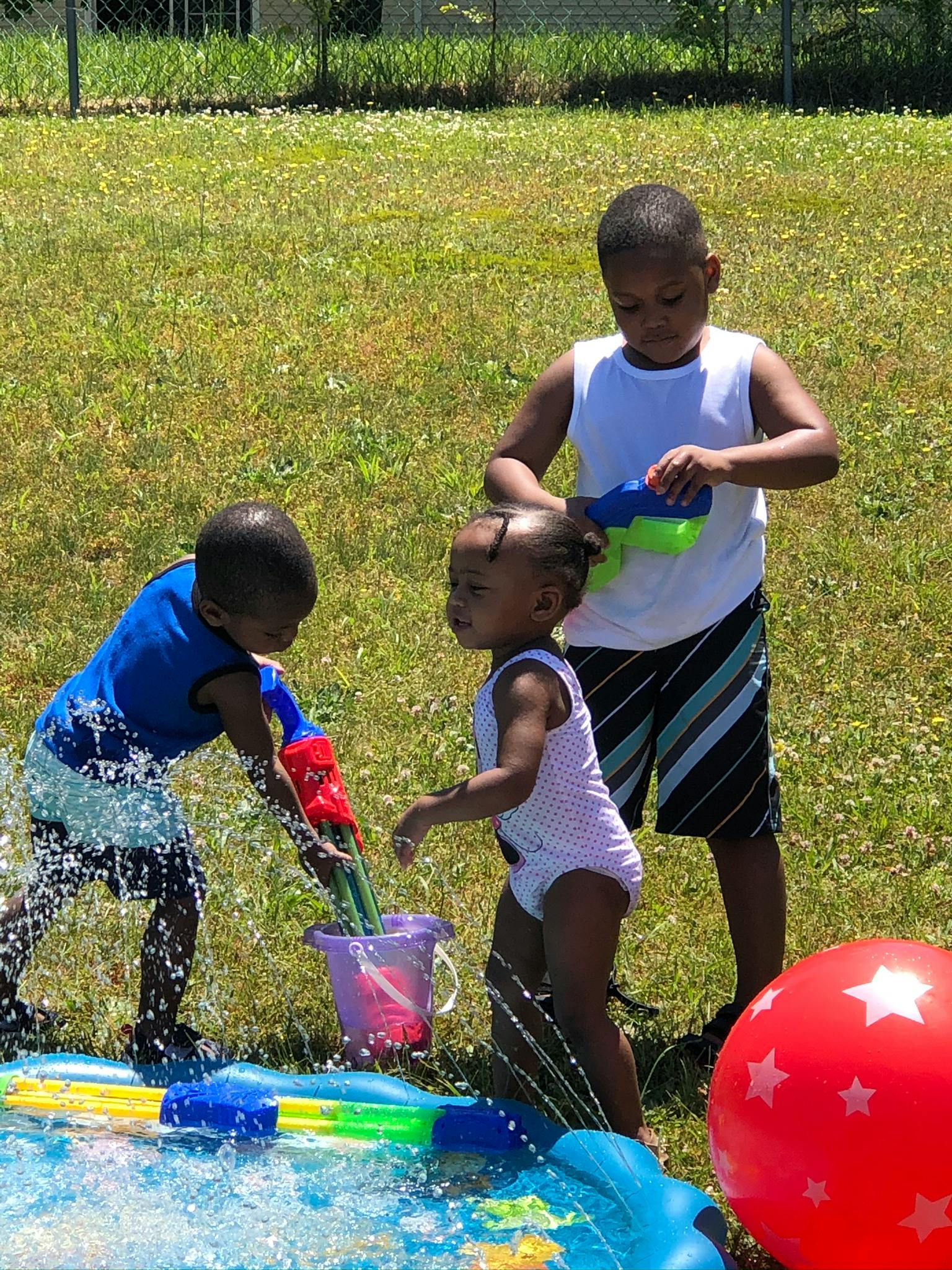 Three children playing with water toys in a grassy area